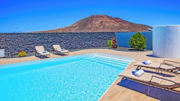Piscina com espreguiçadeiras, parede de pedra e montanha ao fundo.