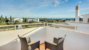 A balcony with wicker chairs and a view of the sea and buildings.