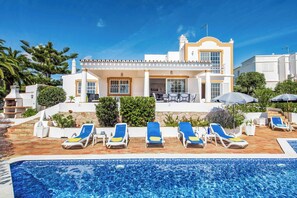 Een witte villa met een zwembad, ligbedden en een overdekt terras.