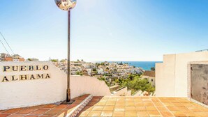 A street sign for Pueblo Alhama with a view of a coastal town and the sea in the background. - Villa Clarence (Nerja)