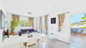 A bright living room with a sofa, a dining table with chairs, and a view of the outside. - Villa Clarence (Nerja)