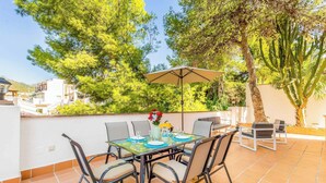 An outdoor patio with a glass table, chairs, and a beige umbrella. - Villa Clarence (Nerja)