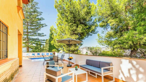 An outdoor patio with a pool, seating area, and a view of trees. - Villa Clarence (Nerja)