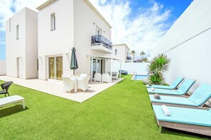 Una villa moderna con un patio que cuenta con piscina, sillones de descanso y un comedor.