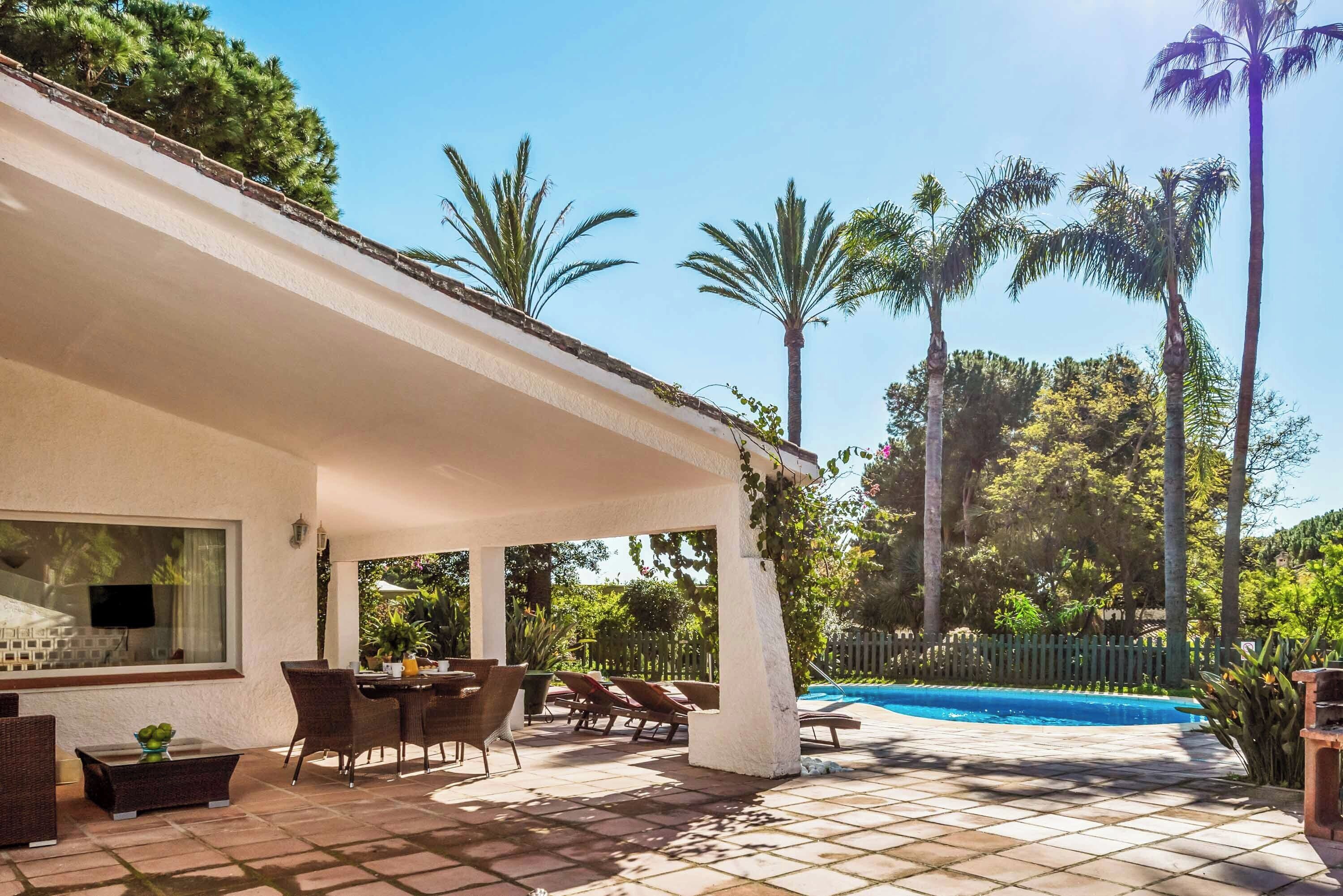 A covered outdoor patio with a pool, surrounded by palm trees and a tiled floor.