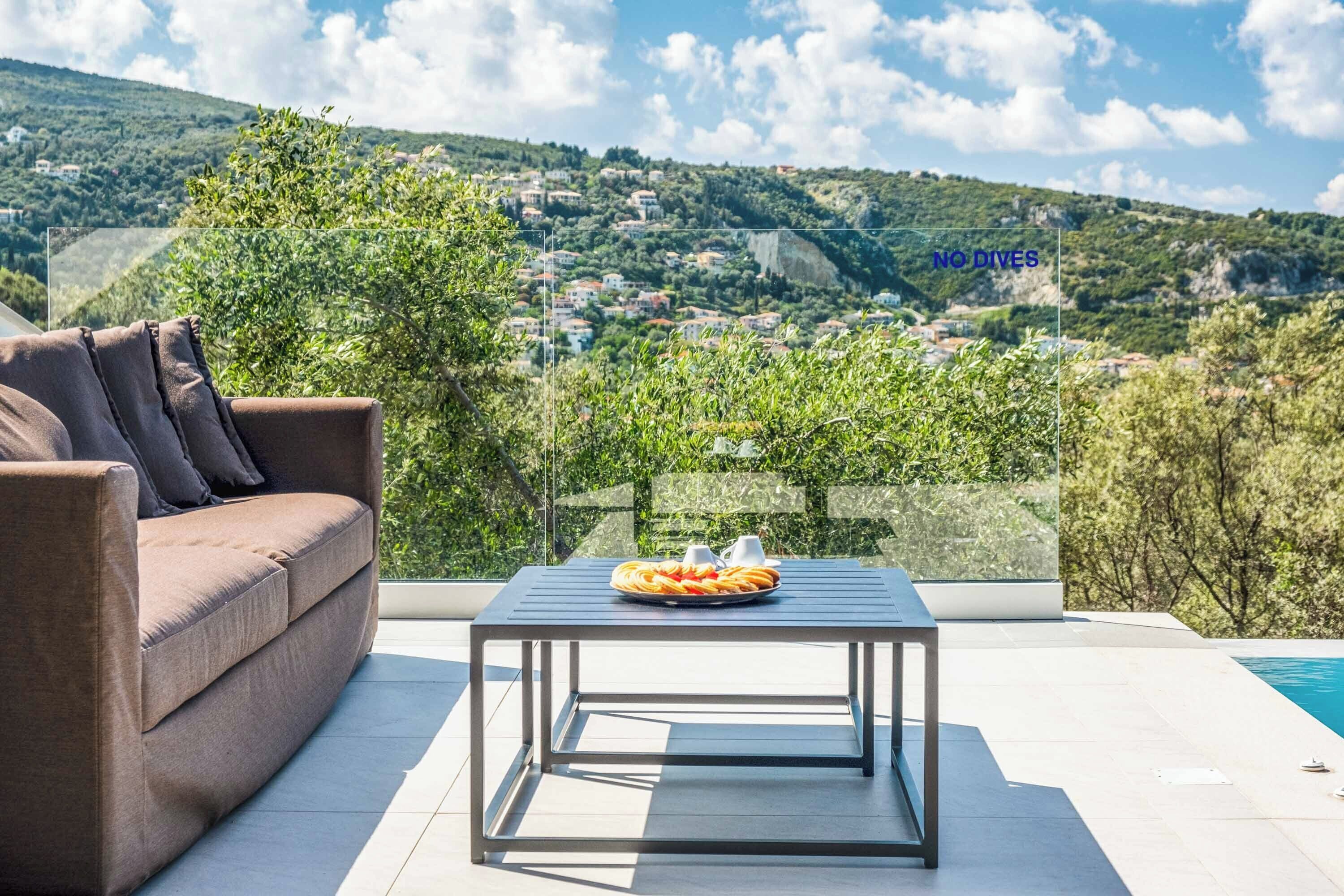 A modern outdoor seating area with a sofa and a table, overlooking a scenic hillside view.