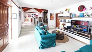 A modern living room with teal sofas, a flat-screen TV, and a dining area with a chandelier. - Villa Dos Piedras (Tías)