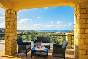 A balcony with stone pillars, wicker furniture, and a table with a bottle and glasses.