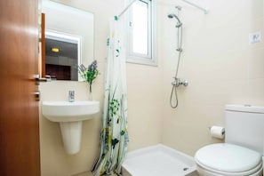 A bathroom with a sink, toilet, shower, and a window.