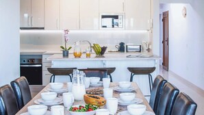 A modern kitchen with white cabinets, a central island with a sink, and a dining area with a wooden table set for four. - Vista Rey (Yaiza)