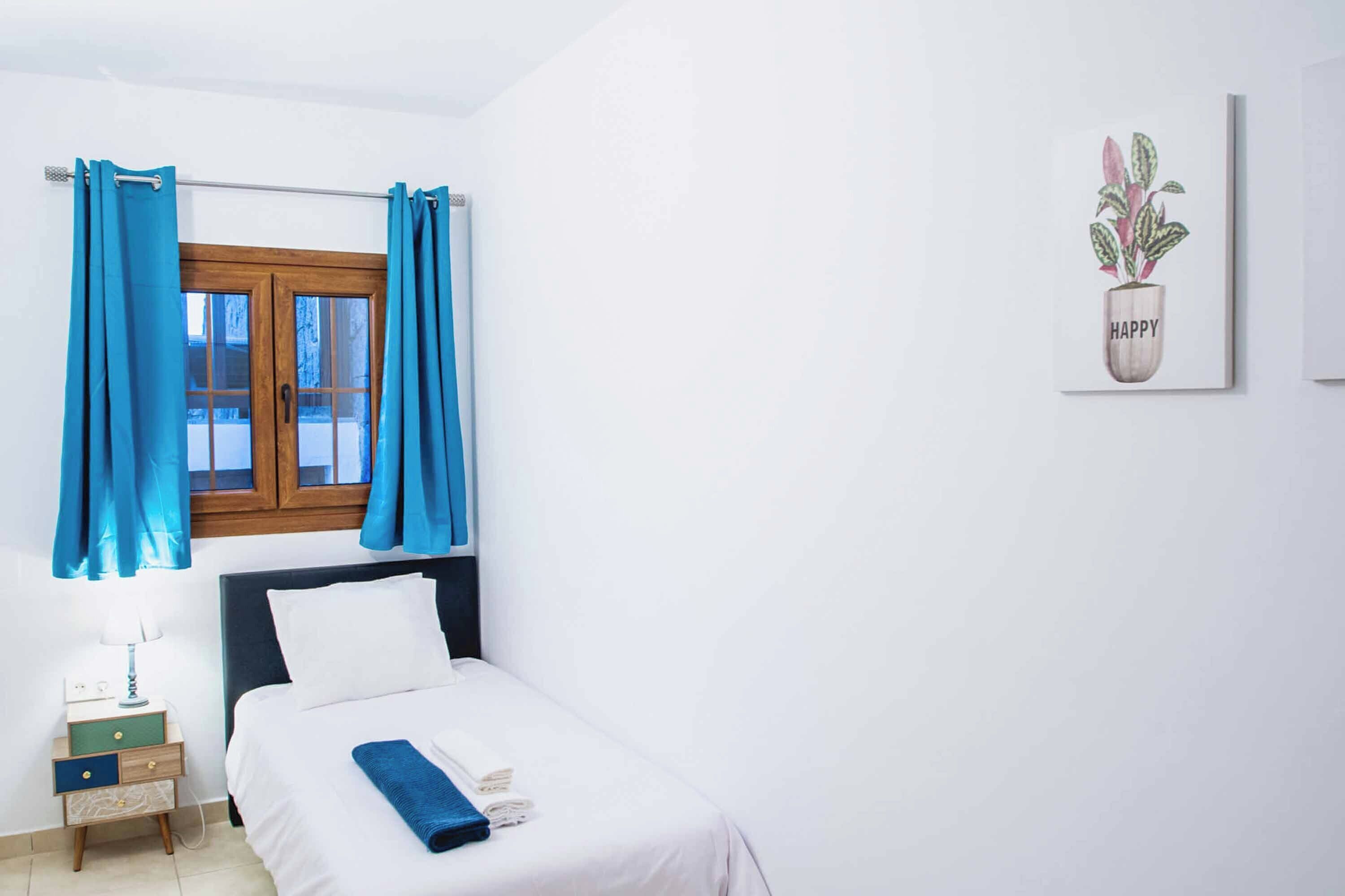 Une chambre à coucher avec un lit, une table de chevet, une fenêtre avec des rideaux et un mur orné d’une plante.