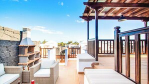 A patio area with outdoor furniture, a stone wall, and a view of the surrounding landscape. - Vista Rey (Yaiza)
