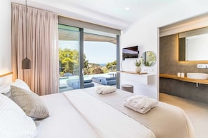 A modern hotel room with a large bed, a bathroom with a mirror and sink, and a view of the outdoors. - Villa Beyond the Dream (Lefkada)