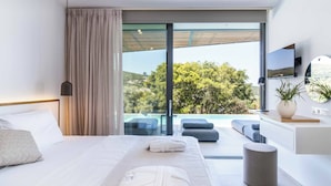 A modern bedroom with a large bed, a view of a pool and greenery, and a mounted TV. - Villa Beyond the Dream (Lefkada)