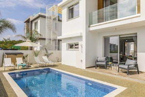 A modern poolside area with a clear blue pool, white lounge chairs, and a covered seating area.