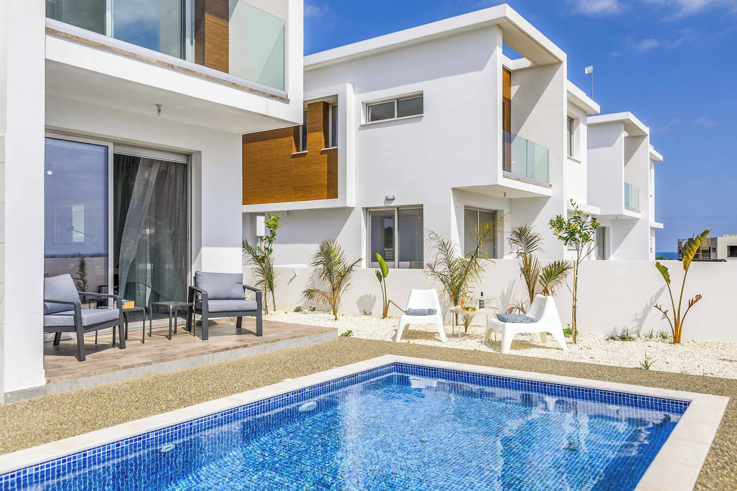 Ein modernes Hotel mit Pool, Sitzgelegenheiten im Freien und heller Fassade.