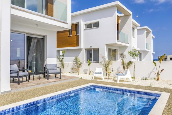 A modern hotel with a swimming pool, outdoor seating, and a white exterior.