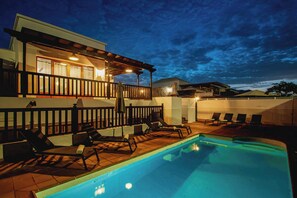 Una casa moderna de dos pisos con piscina, mobiliario exterior y un patio cubierto.