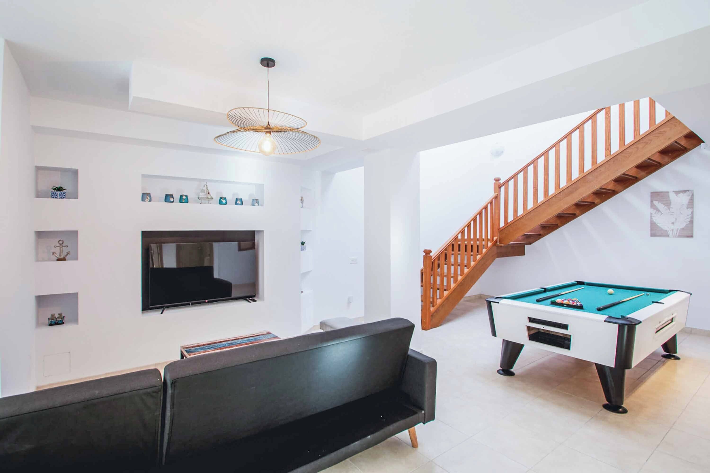 Una sala de estar moderna con una mesa de billar, un sofá, un televisor y una escalera.