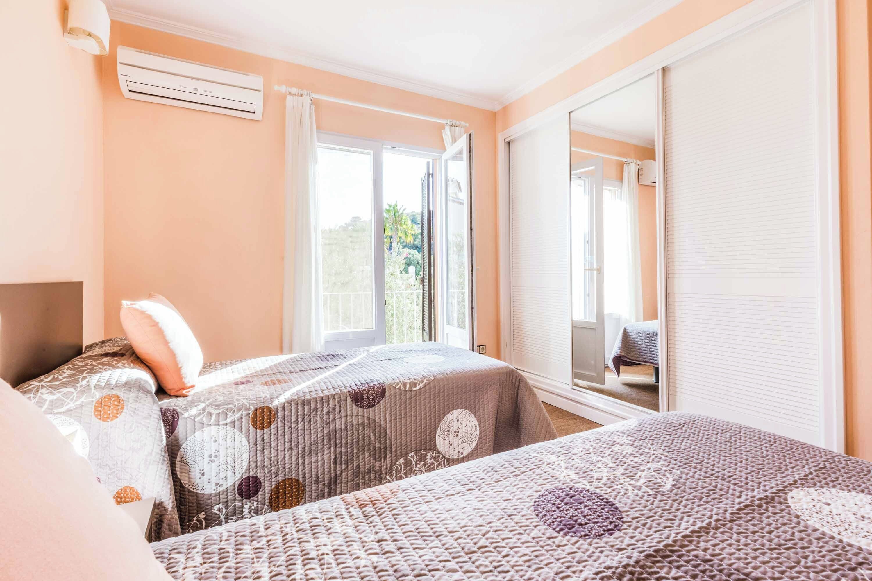 Un dormitorio con dos camas, un equipo de aire acondicionado, un ventanal con cortinas y una puerta corredera.