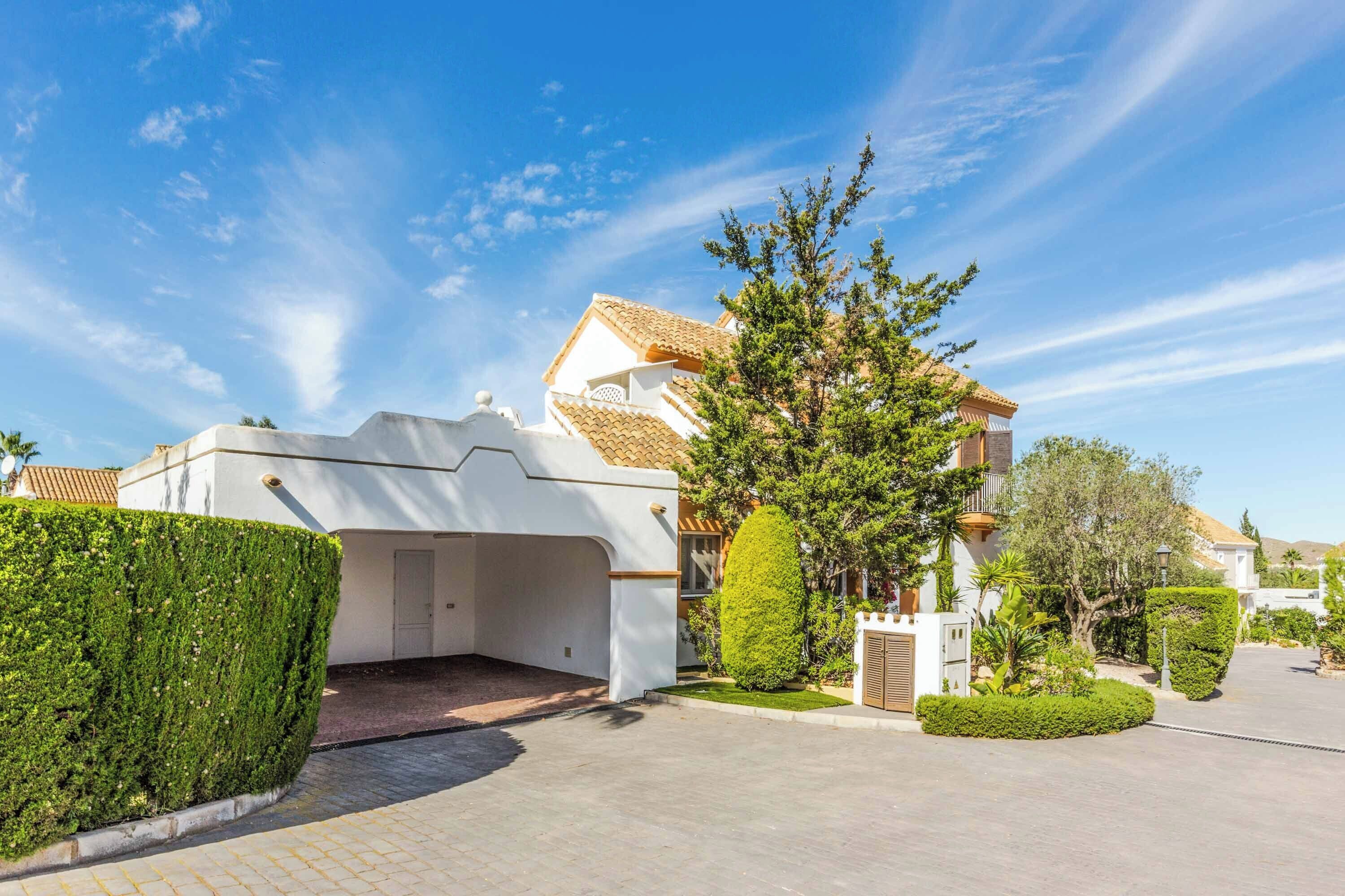 Un edificio moderno con facciata bianca, tetto in tegole e un giardino curato con siepi e alberi.
