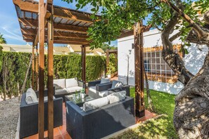 Un patio al aire libre con mobiliario de mimbre, una pérgola y un árbol grande.