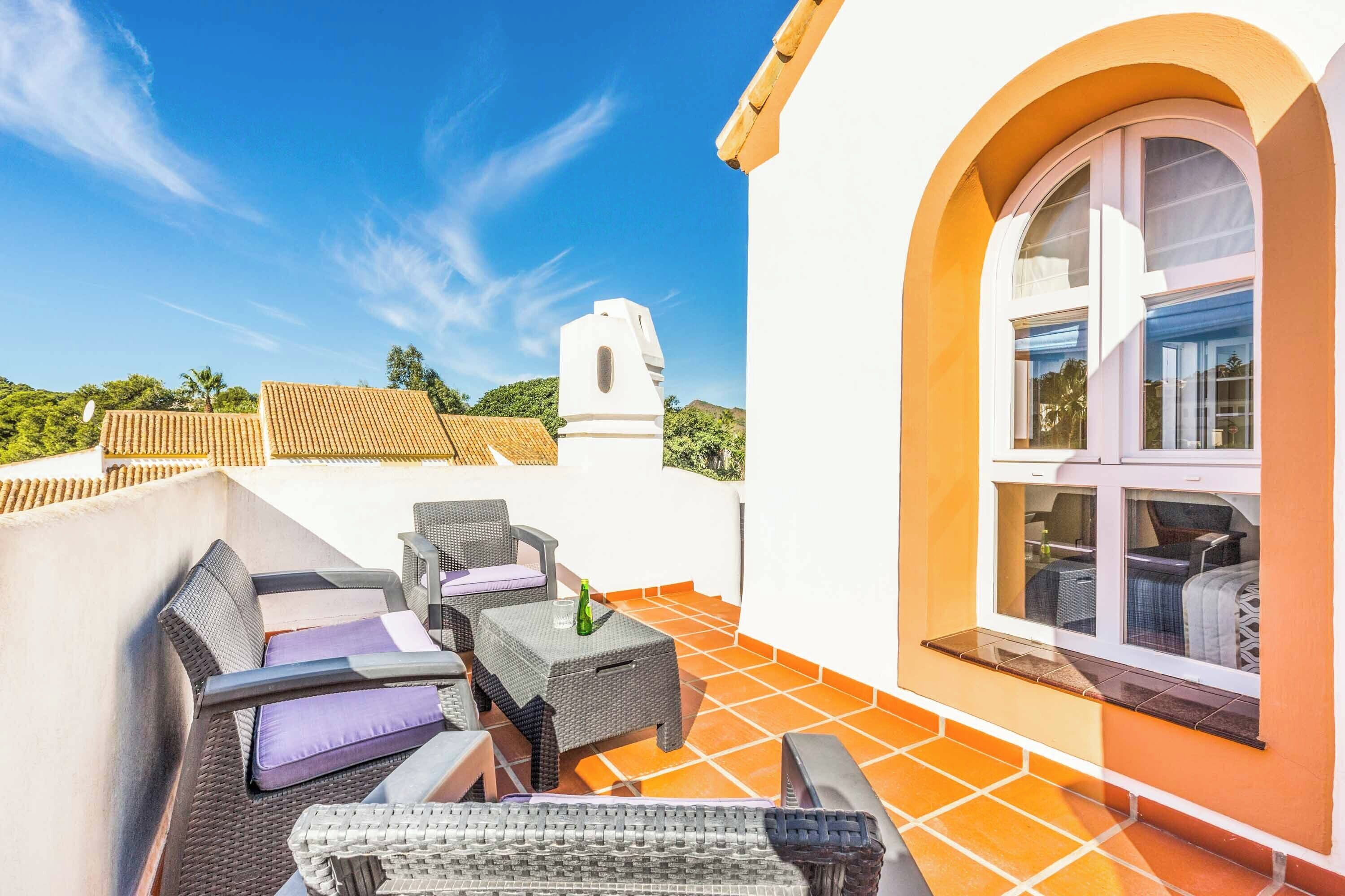 Terraço no telhado com móveis de vime, piso de azulejos e vista para a paisagem ao redor.