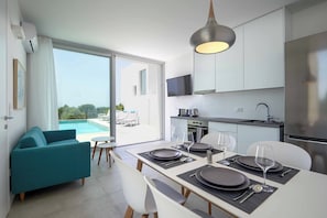 A modern kitchen with a dining area, a TV mounted above the counter, and a view of a swimming pool.