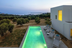 A modern outdoor pool area with lounge chairs and a view of the sea.