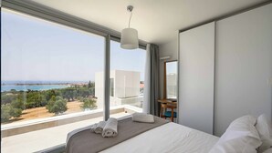 Una habitación de hotel moderna con un ventanal amplio que ofrece vista al mar y edificios.