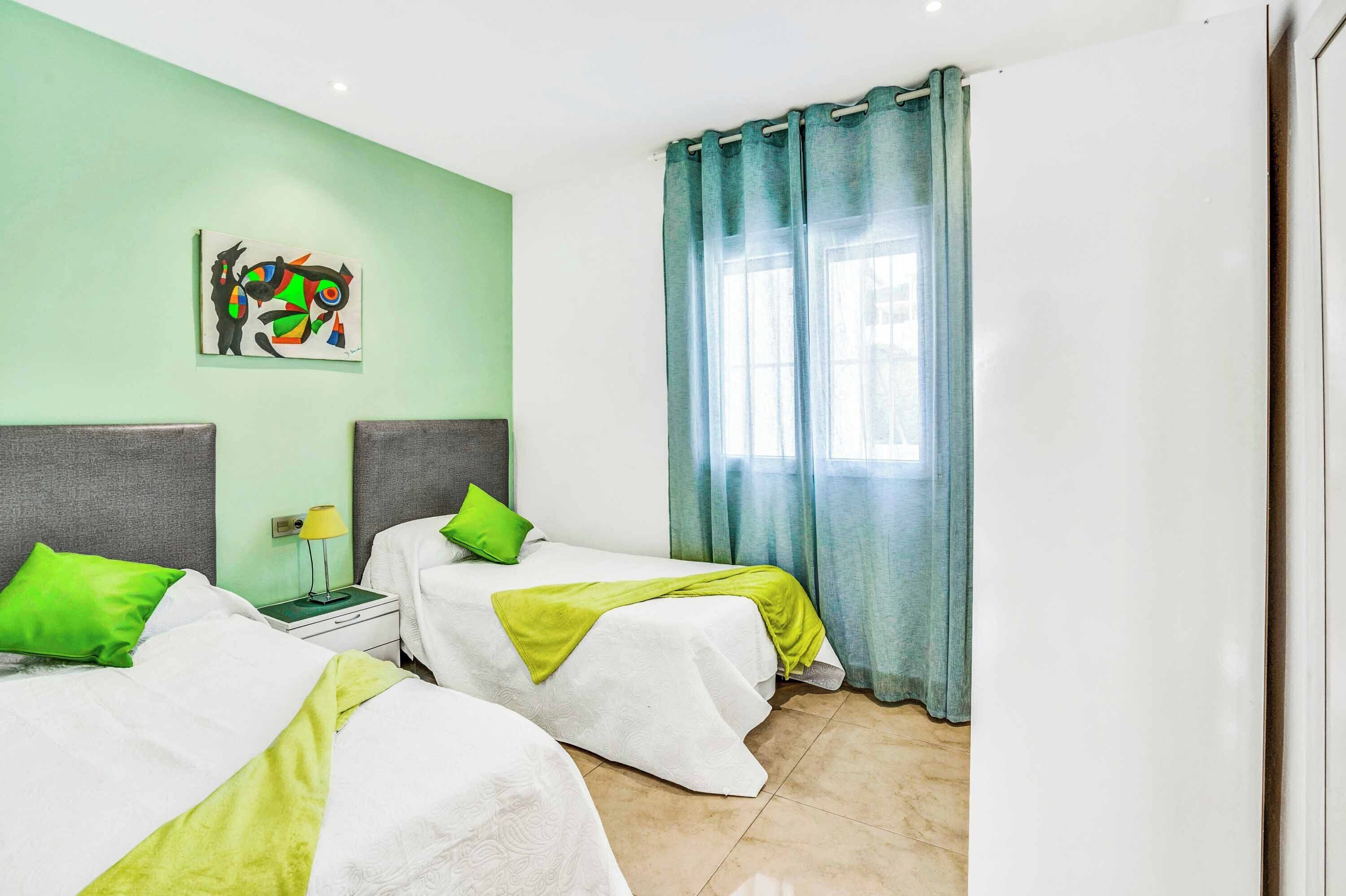 Habitación de hotel con dos camas, almohadas verdes, un cuadro en la pared y una ventana con cortinas.