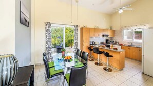 A modern kitchen with a dining area, featuring a glass table, black chairs, and a ceiling fan. - Villa Kampos (Pegeia)