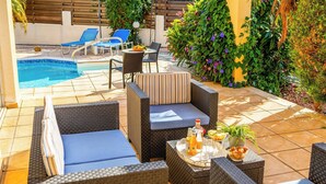 A poolside area with wicker furniture, a table with drinks, and a view of the pool. - Villa Kampos (Pegeia)