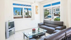 Ein modernes Wohnzimmer mit Glastisch, grauem Sofa und Flachbildfernseher.