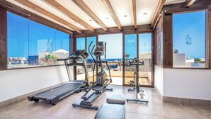 A gym with treadmills, elliptical machines, and weight benches, featuring large windows with a view of the sea. - Villa Xian (Yaiza)