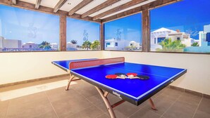 A ping pong table with paddles in a room with large windows and wooden beams. - Villa Xian (Yaiza)