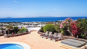 A pool area with lounge chairs and a view of the sea and distant buildings. - Villa Buena Vista Bocaina (Yaiza)