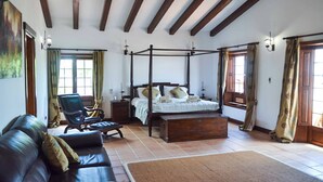 A bedroom with a four-poster bed, a wooden bench, a leather sofa, and a chair. - Villa Buena Vista Bocaina (Yaiza)