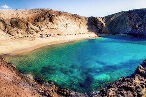 Un paysage côtier caractérisé par une eau turquoise et limpide, des falaises rocheuses et une plage de sable.