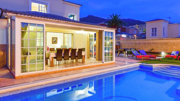 Una casa moderna con piscina, comedor y patio con sillones de descanso.