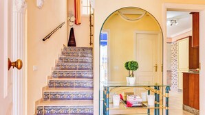 Una escalera con baldosas de diseño azul y blanco, una mesa de vidrio con detalles dorados y una pequeña planta en maceta.