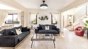 A spacious living room with a sofa set, a coffee table, and a red chair. - Villa Cleco (Pegeia)