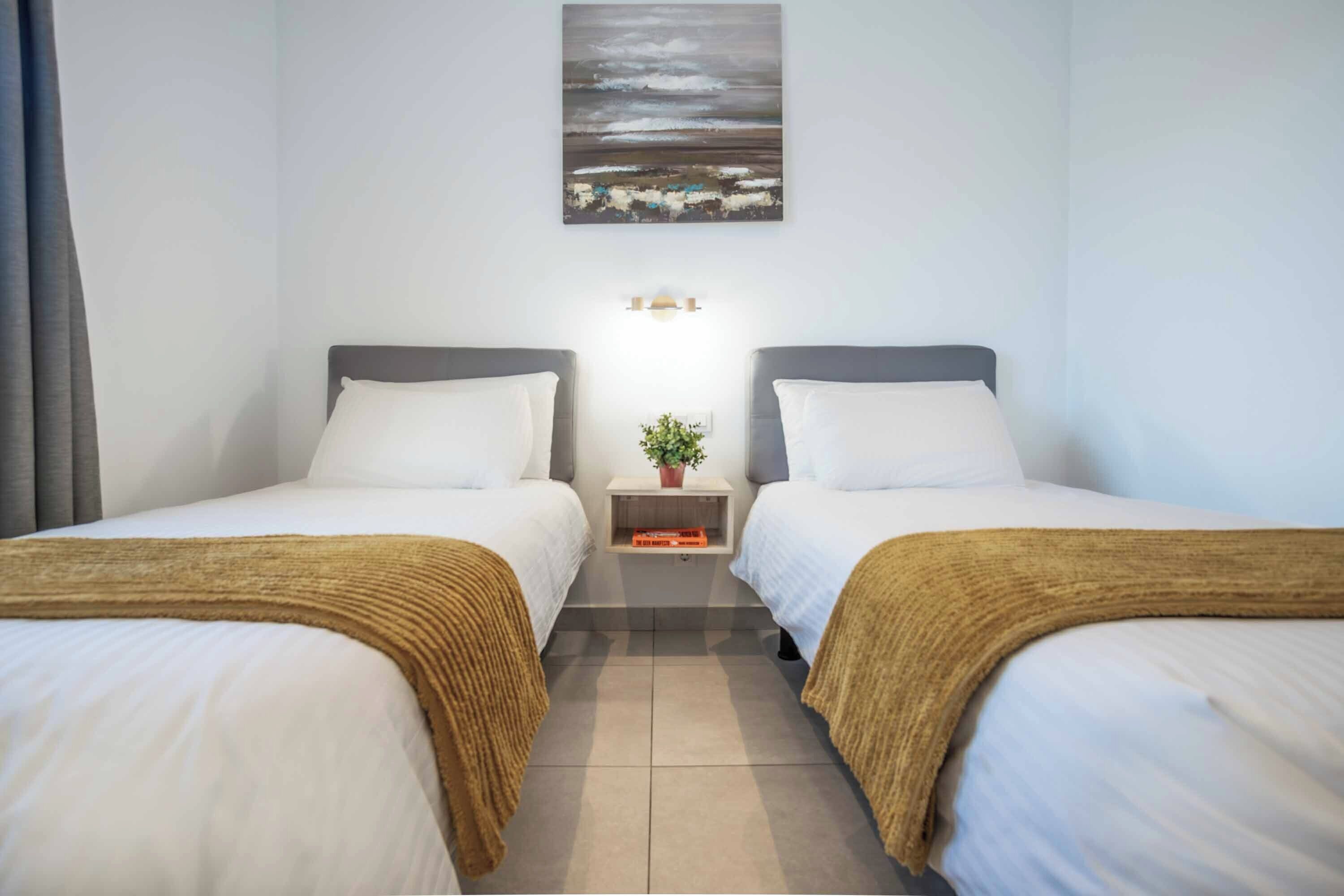 Une chambre d’hôtel avec deux lits, une table de chevet ornée d’une plante et un tableau accroché au mur.