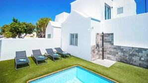 A modern white building with a swimming pool, lounge chairs, and a stone wall. - Villa Mi Deseo (Tías)