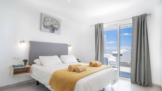 A modern bedroom with a bed, bedside table, and a view of the sky through a glass door. - Villa Mi Deseo (Tías)