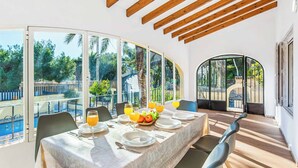 A dining area with a table set for four, large windows, and a view of the outdoors. - Villa Enzo Moraira (Teulada)