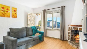 Una sala de estar acogedora con un sofá gris, una chimenea y un amplio ventanal con cortinas.