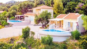 A residential area with houses, a swimming pool, and a hillside with trees. - Villa Baby Lemoni (Kefalonia)