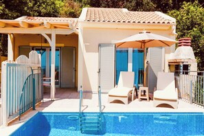 A pool area with a clear blue pool, a ladder, lounge chairs, and an umbrella. - Villa Baby Lemoni (Kefalonia)