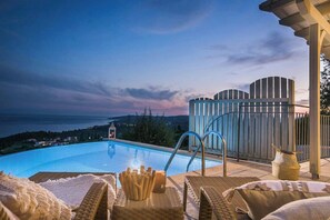 A swimming pool with lounge chairs and a view of the sea at dusk. - Villa Baby Lemoni (Kefalonia)